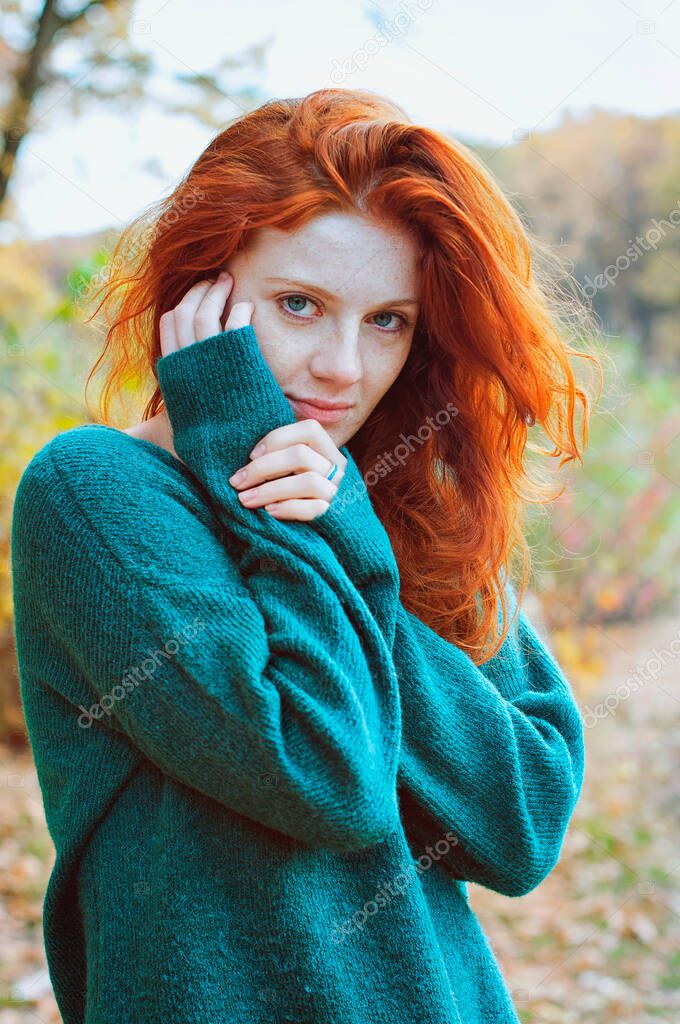 Portrait of a beautiful red-haired girl with freckles and blue eyes in autumn park