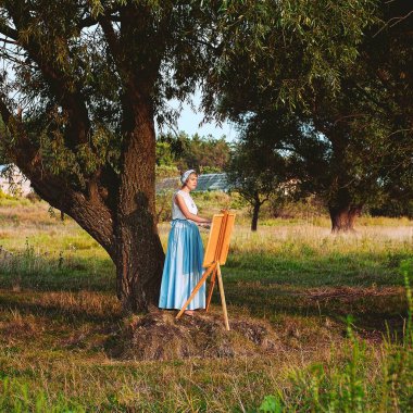 Günbatımında tek başına zarif bir sanatçı göl kenarında doğanın bir resmini çizer.