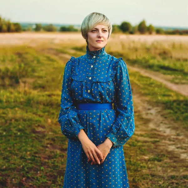 Doğada yürüyen mavi elbiseli zarif, mutlu bir bayan.