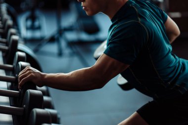 Spor salonunda dambıllarla sırtını çalıştıran güçlü bir adam.