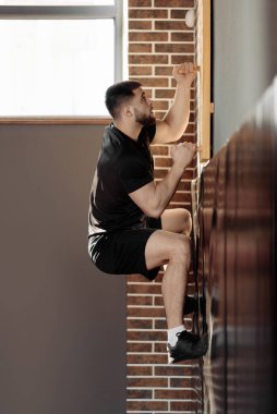 Spor salonunda tahta duvara tırmanan bir adam.