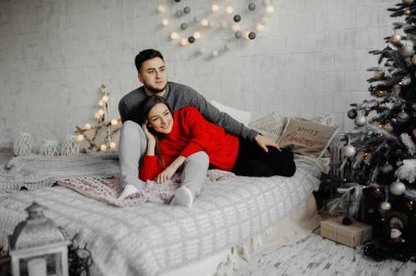 Kışlık kazak giyen neşeli çift rahat bir yatakta uzanıp gülüyor.