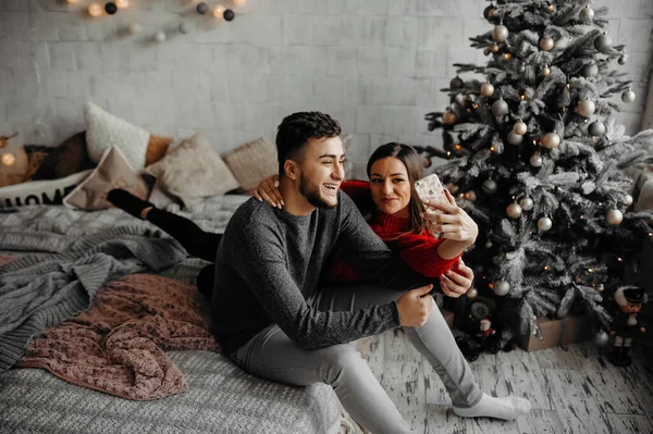 Szczęśliwa młoda para robi selfie w domu, bawiąc się i śmiejąc blisko choinki — Zdjęcie stockowe