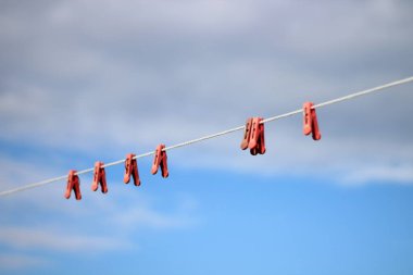Parlak mavi gökyüzü ve beyaz bulutlara karşı kırmızı plastik mandallı çamaşır ipinin fotoğrafı