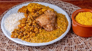 Traditional Afro Brazilian dish made with okra and dried shrimp accompanied by vatap, beans, rice, chicken and manioc flour on a wooden table. clipart