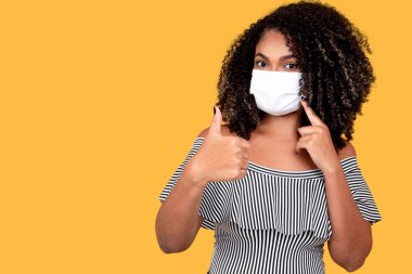 Koruyucu tıbbi maskeli genç siyahi bir kadının stüdyo portresi. Corona gribi salgını, Covid 19 'da kopya için yer var..