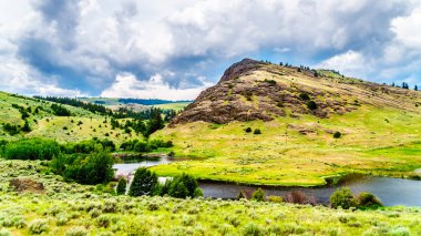 Rocky Mountain among the rolling hills in the Nicola Valley along Highway 5A between Merritt and Kamloops, British Columbia, Canada under dark cloudy skies clipart