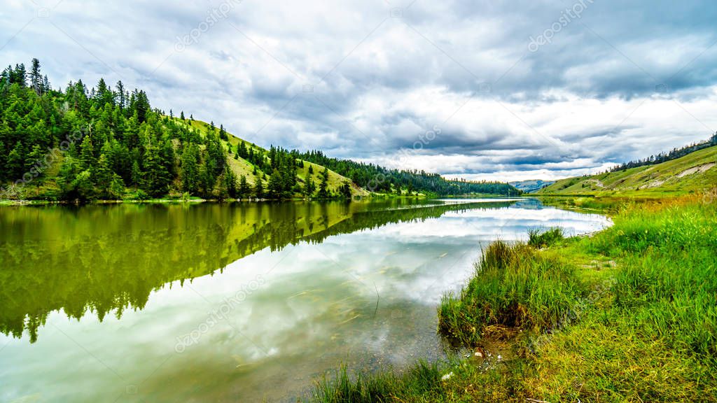 Dark Clouds and surrounding Mountains reflecting on the smooth water surface of Trapp Lake, located along Highway 5A between Kamloops and Merritt in British Columbia, Canada