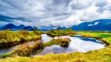 Dark rain clouds on a cold spring day at over the Pitt River and the lagoons of Pitt-Addington Marsh in Pitt Polder near Maple Ridge in British Columbia, Canada  clipart