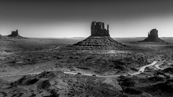 Black and White Photo showing the gravel road winding around East and West Mitten Buttes in the desert landscape in Monument Valley Navajo Tribal Park in southern Utah, United States