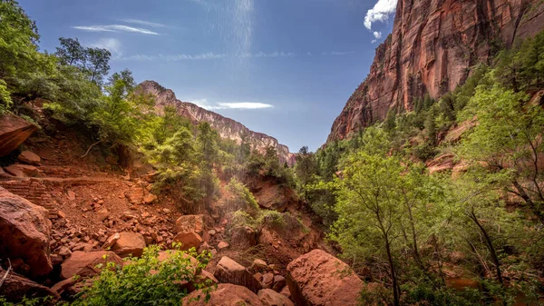 A small Waterfall flowing over the Cliffs overhanging the Trail and Rock Slide of the Lower Emerald Pool Trail in Zion National Park, Utah, United States