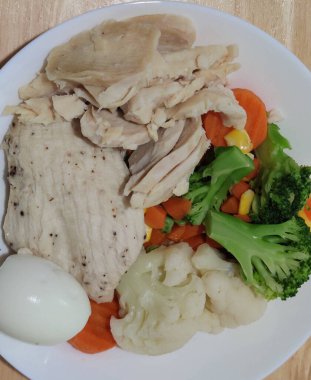 Dilimlenmiş orta pişmiş yumurta ve çeşitli sebzelerle servis edilen organik tavuk göğsü beyaz tabak, ev yapımı, taze market restoranı, yemek menüsü reklam geçmişleri üzerine havuç, bezelye brokoli.