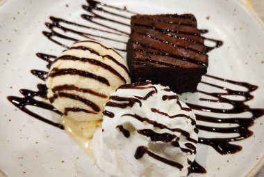 Yakın plan çikolatalı lav keki şuruplu ve vanilyalı tatlı dondurma sosuyla süslenmiş beyaz seramik tabakta fusion gurme kafe restoranında, yemek stilisti.