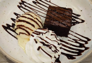 Yakın plan çikolatalı lav keki şuruplu ve vanilyalı tatlı dondurma sosuyla süslenmiş beyaz seramik tabakta fusion gurme kafe restoranında, yemek stilisti.