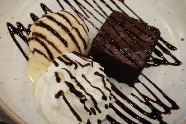 Yakın plan çikolatalı lav keki şuruplu ve vanilyalı tatlı dondurma sosuyla süslenmiş beyaz seramik tabakta fusion gurme kafe restoranında, yemek stilisti.