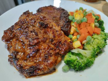 Dilimlenmiş organik domuz eti, çeşitli rengarenk sebzelerle süslenmiş biftek, ahşap masada beyaz tabakta servis edilen bezelye aromalı limon sosu, sokak yemekleri restoranının ünlü gizli tarifi, yemek stilisti.