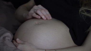 Yatakta karnına dokunan hamile bir kadın. 4k.