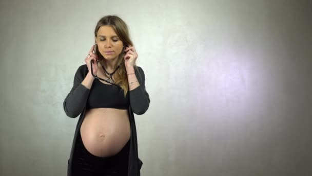 年轻的孕妇用听诊器听她的腹部 — 图库视频影像