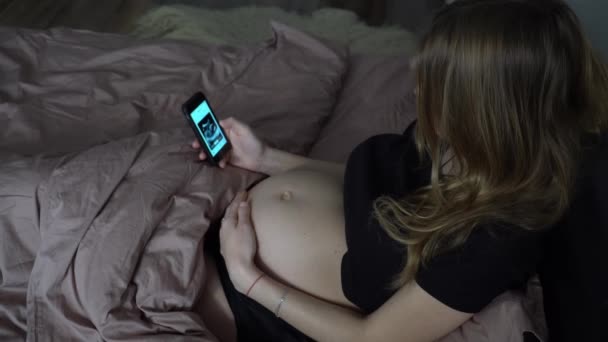 妊娠中の女性は スマートフォン上の超音波写真を見ます — ストック動画
