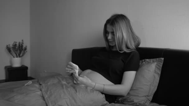 Mladá těhotná žena se dívá na oblečení pro své nenarozené dítě. 4k