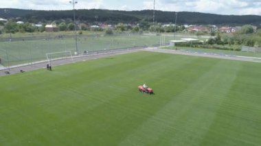 Bir futbol sahasının bakımı. Çim biçme makinesi yeşil çimenler kesiyor. Havadan görünüm. 4k