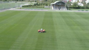 Bir futbol sahasının bakımı. Çim biçme makinesi yeşil çimenler kesiyor. Havadan görünüm. 4k
