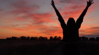 Gün batımında kızın sevinçle ellerini kaldırdığını gösteren yavaş bir görüntü. 