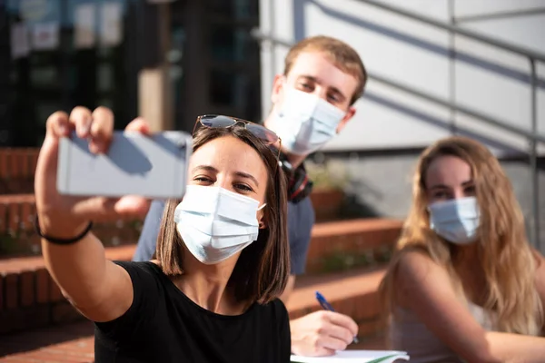 Coronavirus ya da covid-19 salgını sırasında yüz maskesi takan üç üniversite öğrencisi selfie çekiyor..