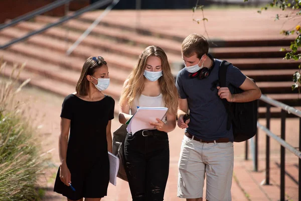 Coronavirus salgını sırasında kampüste yürürken maske takan üç üniversite öğrencisi sohbet ediyor..