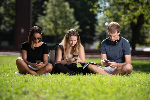 デジタル技術中毒の概念 3人の大学生が携帯電話でおしゃべりをしている — ストック写真