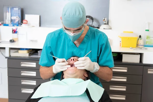 Dentist wearing double mask making a basic check up to a female patient during coronavirus pandemic.