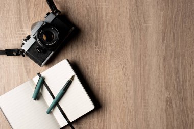 Analog vintage bir kamera, bir defter ve tahta bir masa üzerinde fotokopi alanı olan bir kalem..