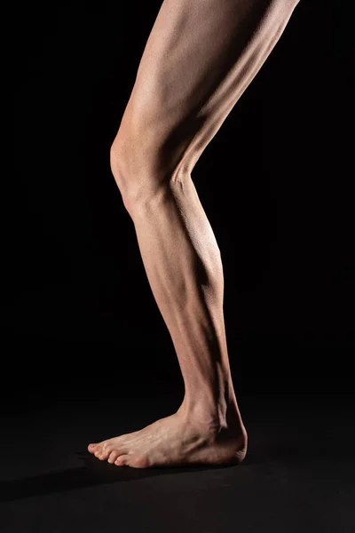 Çıplak ayaklı bir bisikletçinin bacak ve baldır kaslarının yan görüntüsü. Stüdyo fotoğrafçılığı siyah arkaplan