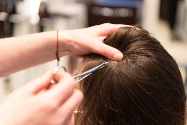 Bir saç stilistinin yakın plan çerçevesi analiz edilecek bir müşteriye saç ayıklıyor.