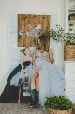 güzel bir hamile kadın ve küçük kızı aynı mavi elbise ve yeşil çizmeler gülümseyen, gibi bir anne gibi bir kızı