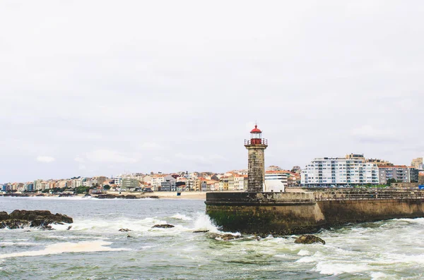 Old stone Porto lighthouse near ocean and Porto cityscape