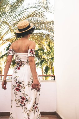 Moda gözlüklü, şapkalı ve kumsalda uzun elbiseli genç bir kadın. 