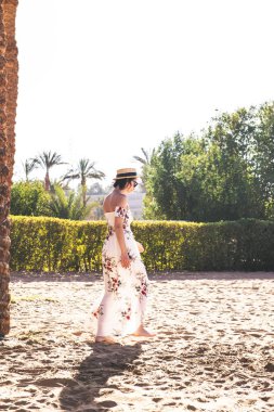 Moda şapkalı kadın ve plajda palmiyelerin yanında giyinen kadın. 