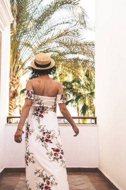 Moda gözlüklü, şapkalı ve kumsalda uzun elbiseli genç bir kadın. 