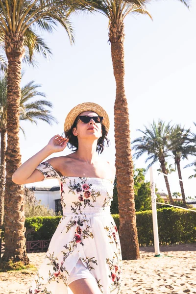 Mulher de vestido longo e chapéu andando na areia perto do oceano — Fotografia de Stock