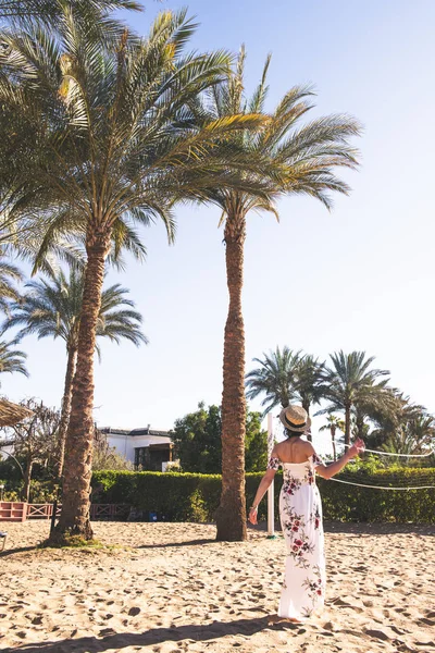 Mulher de vestido longo e chapéu andando na areia perto do oceano — Fotografia de Stock