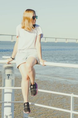 Genç bir kadın okyanusun kenarında oturuyor ve ileriye bakıyor. 