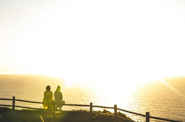 Les gens assis et regardant vers l'avant près de l'océan pendant le coucher du soleil — Photo