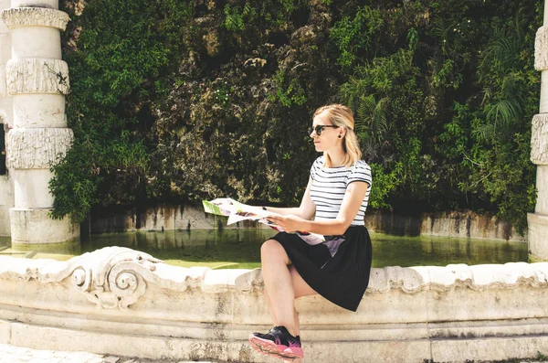 Молодая женщина сидит рядом с историческим фонтаном с картой и поиска — стоковое фото