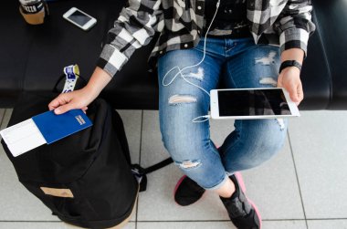 Kadın elinde pasaport, tablet ve kahve ile bekliyor.