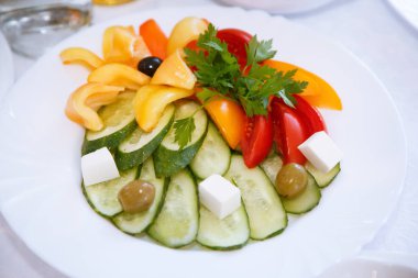 Sebze güzel beyaz bir tabak üzerinde dilimlenmiş. Salatalık, kırmızı domates, sarı dolmalık biber, zeytin, zeytin, peynir küpleri, maydanoz yaprak güzel hizmet. Üstten görünüm.