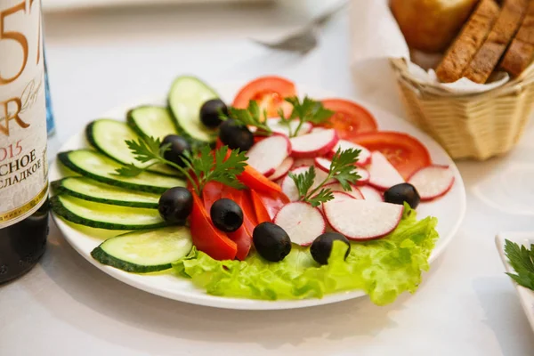 Vegetables beautifully sliced on a white dish. Cucumber, red tomato, red bell pepper, olives, radish, parsley leaf beautifully served on a leaf of green salad. Side view. Close up.