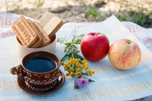 Output. Vacation. Rest. Clay Cup and saucer. Cup of coffee. Black coffee. Cookies and waffles. Flowers. Close up. Side view. Red and pink apples. Light background. Breakfast in nature. Lunch out. Breakfast outside the home.