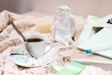 Bir kitap, bir dizüstü bilgisayar, bir fincan sade kahve, şeker fıstık, bir mum, yumuşak, bej battaniye üzerinde sıva bir melek heykeli faux kürk ürünleri. Yan görünümü. loseup.