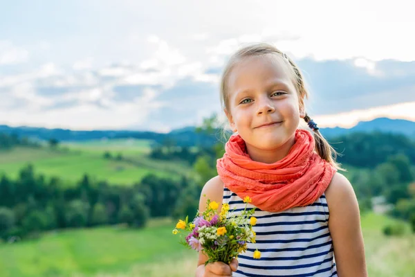 山の風景の背景の野生の花の花束を持つ少女の笑みを浮かべてください — ストック写真